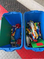 Two blue LEGO storage tubs containing assorted bricks and baseplates, open lid showing contents
