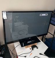 Full front view of LG 50-inch TV on stand showing screen and some cables around base. TV screen shows 'No Signal' message.