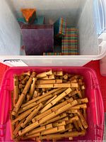 Pink plastic container filled with vintage wooden Lincoln Logs showing logs with notches and cylindrical shapes.