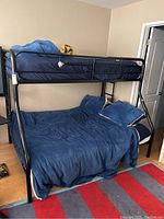 Full view of the bunk bed showing full lower bed with blue bedding and twin size upper bed with blue bedding and basketball plush.