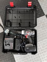 Open black plastic carrying case containing Porter Cable cordless drill, battery, charger, and some screws.