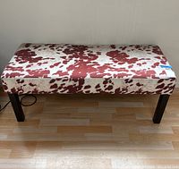 Upholstered bench viewed frontally showing the patterned upholstered seat and dark wooden legs.
