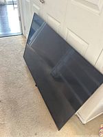 Vizio 55 inch TV screen leaning against door on carpet floor, showing the screen surface and black frame.