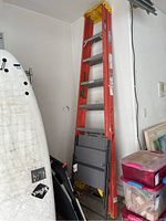 Full view of Werner orange fiberglass ladder standing upright with folding chair folded and resting against it