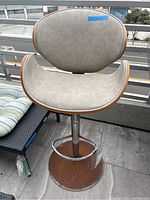 Front view of the swivel bar chair showing the light neutral fabric seat and backrest with wood frame and rusted metal base.