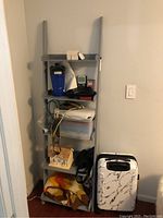 Front view of 5-tier gray wooden open shelf with various items placed on shelves, next to white wall and door