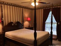 Four poster bed in a bedroom with mattress on frame, showing wood carved posts and headboard.