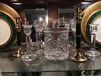 Wide shot showing cut glass biscuit jar with lid, two pairs of clear glass candlesticks, and two green brass gallery candlesticks.
