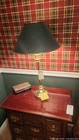 Brass table lamp on a wooden table showing green shade and brass base against plaid wallpaper background.