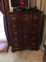 Front view of dark wooden chest with five drawers showing brass handles and carved shell decoration on top drawer.