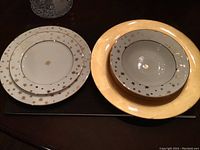 Full view of sample dinner plate, salad plate, soup bowl, and gold ceramic charger showing gold star and floral gold trim design.
