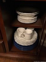 Stack of plates, cups on top, and blue ceramic chargers at bottom in cabinet