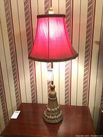 Front view of one lamp showing red fabric shade and detailed braided metal base