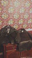 Two black leather jackets hung on furniture against red floral wallpaper.
