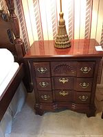 Front view of wooden three drawer nightstand with brass handles and scallop shell decor on one drawer.