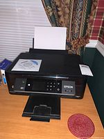 Front and top view of Epson XP-440 printer on wooden table showing paper input tray, control panel, and Epson branding.