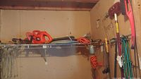 Overview of the lot on a shelf in a shed showing various tools including Black+Decker electric chainsaw, cords, and garden tools