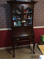 Full view of the tall wooden secretary desk showing glass doors, closed fold-down writing surface, and drawer below.
