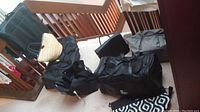 Photo of multiple black leather and canvas duffel bags, a woven bag, and a black felt bag on carpeted floor