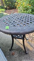 Close-up photo of the round metal outdoor table top showing lattice open design with decorative border.