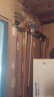 Photo showing long-handled metal rake, leaf rakes, and various garden tools hanging on wall inside shed