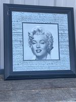 Framed black and white photographic print of Marilyn Monroe. Frame is square black wood with some scratches and distressed border mat.