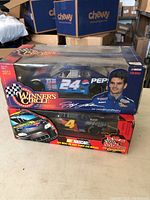 Two NASCAR diecast cars in original packaging, blue Dale Earnhardt Jr. #24 Pepsi car on top and black and red #4 Kodak car underneath, both boxes show age.