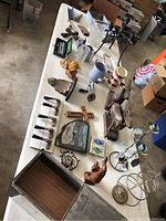 Wide angle view of a table filled with varied vintage items showing a mix of decorative objects including a metal rack, wood carvings, ceramic items, a pitcher, and other collectibles.