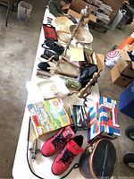 Wide photo showing an assortment of vintage items spread on a table including shoes, games, kitchen and decorative items.