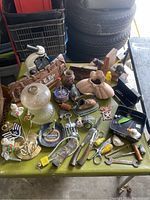 Wide top-down view of diverse small collectibles and household items on green surface including glass globes, metal tools, and decorative wooden pieces