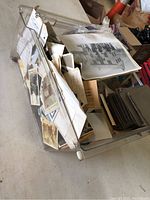 Clear top view of large box filled with old black-and-white photographs and paper ephemera.