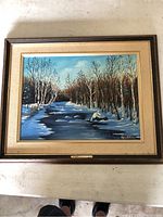 Front view of the framed painting showing a winter river landscape and artist signature.
