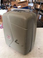 Closed view of the tan/gray hard plastic carrying case for the Revere 8mm projector, showing its shape and built-in handle.