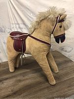 Photo showing side view of light brown plush sit-on toddler horse with maroon saddle and cream faux mane.