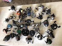Overview of 34 diverse vintage fishing reels laid out on a surface. Includes multiple reel types with varied colors and wear.