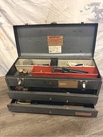 Metal Craftsman toolbox open showing three drawers and red plastic tray inside top lid holding assorted tools and hardware.