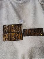 Three vintage Ontario metal vehicle license plates from the 1920s, two dated 1922 and one dated 1928, placed on a white fleece surface.