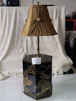Full view of the lamp showing the hexagonal black base, beige pleated shade with button accents, and metal rod connecting base and lampshade.
