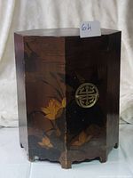 Front view of hexagonal wooden hat cylinder with painted floral motifs and circular metal ornament
