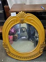 Full view of the oval wall mirror showing carved fan motif top and floral decorations at lower sides with a golden-brown wooden frame.