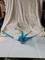 Front view of blue and clear Murano glass centerpiece with three pointed upward arches, sitting on flat surface with neutral fabric backdrop.