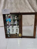 Wooden display case with glass shelves holding multiple porcelain thimbles, door open showing the collection