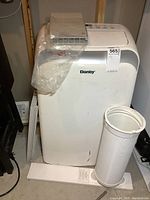 White Danby portable air conditioner unit with hose and vent attachment on floor beside it.