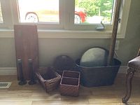 Photo showing large black metal tub, round metal tray, three wicker baskets of varying sizes, and wooden yardstick leaning against window