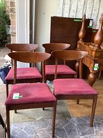 Four mid-century wood framed chairs with reddish upholstered seats seen from an angle showing all chairs together.