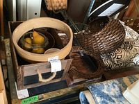Wooden crate with rope handles containing glass bowl with faux fruit, ceramic bowl, and wicker baskets with cushions nearby.