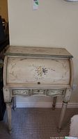 Front view of the vintage painted wood writing desk showing floral designs on the curved roll-top and drawers.