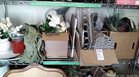 Shelving unit with assorted faux florals, green fabric, cardboard boxes, baskets, and assorted containers.
