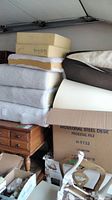 Stack of various foam paddings and cushions including yellow foam blocks, layered foam with batting, and multiple thick white cushions.