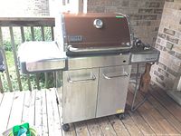 Front view of grill on deck showing stainless steel cart with cabinet and side shelves